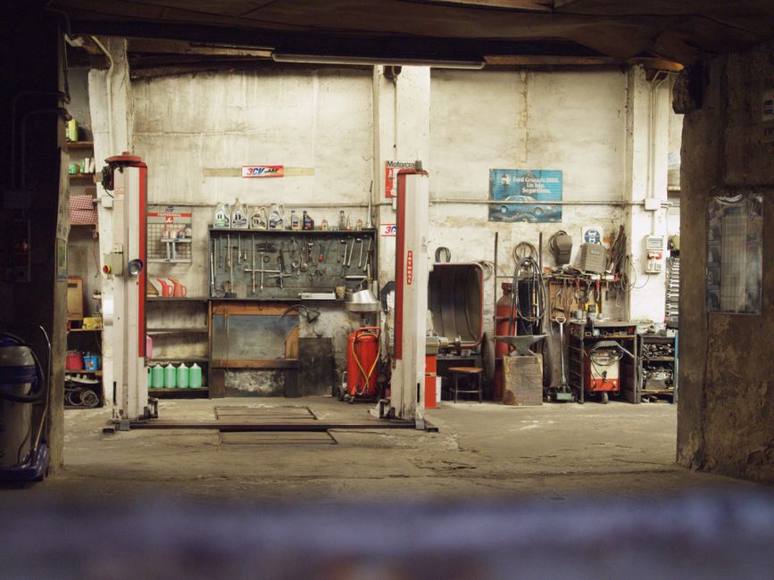 An empty, rustic car workshop featuring tools, machinery, and car lifts in an industrial setting.